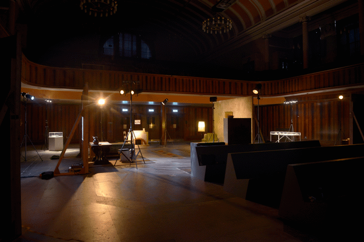 It is a theatre. There are several movie sets built, all illuminated by big spotlights with a warm yellow light. This is part of an art installation in Film City, Glasgow International 2018.