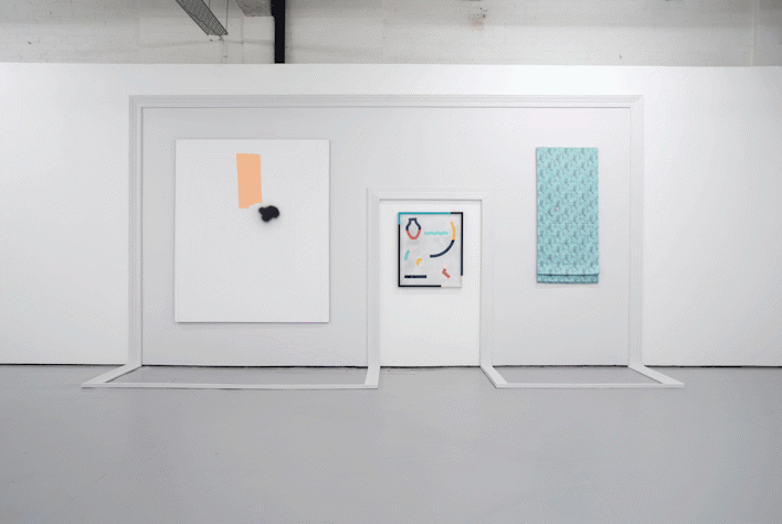A large frame is made around a door, moving onto the floor. The frame has two artworks placed centrally on either sode of the door. One is a cloth and the other is like a painting. On the door, there is a multimedia artwork placed centrally in the top half of it.
