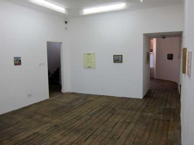installation view of works hung on white walls, with a dark wooden floor