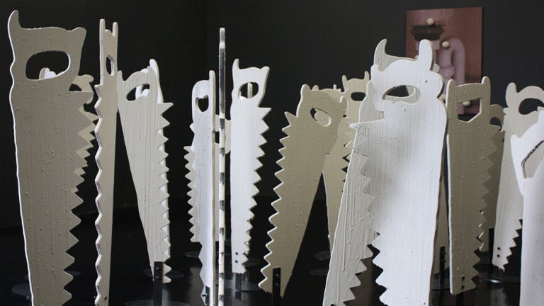 A photograph of a series of sculptures in the shape of simplified hand saws standing on end with a black background