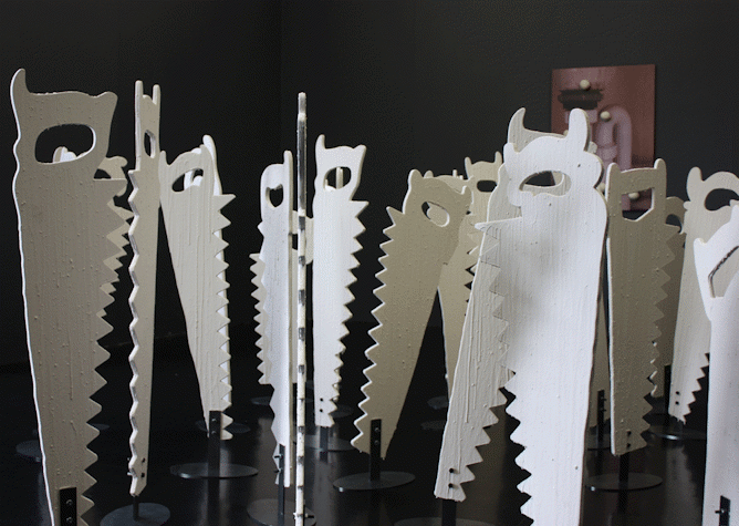 A photograph of a series of sculptures in the shape of simplified hand saws standing on end with a black background