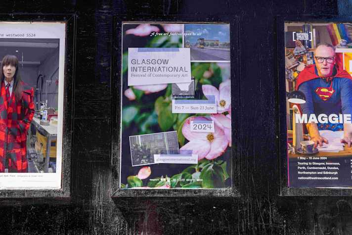 A row of three advertising posters on a wall. The middle poster is for Glasgow International 2024