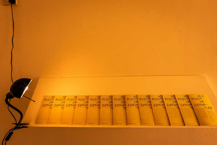 A row of print displayed on a white ledge, lit up by a desk lamp on the left side.