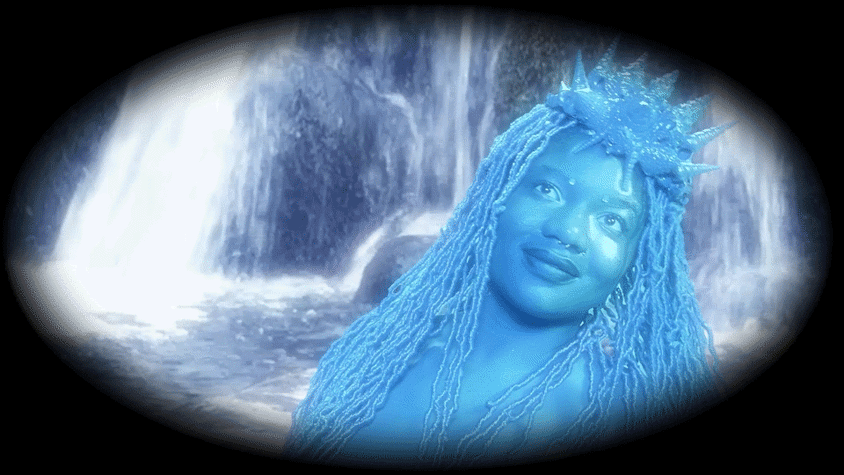 A woman with long braids, wearing a crown, looks upwards in a dreamy fashion. She is painted blue. In the background is a waterfall.
