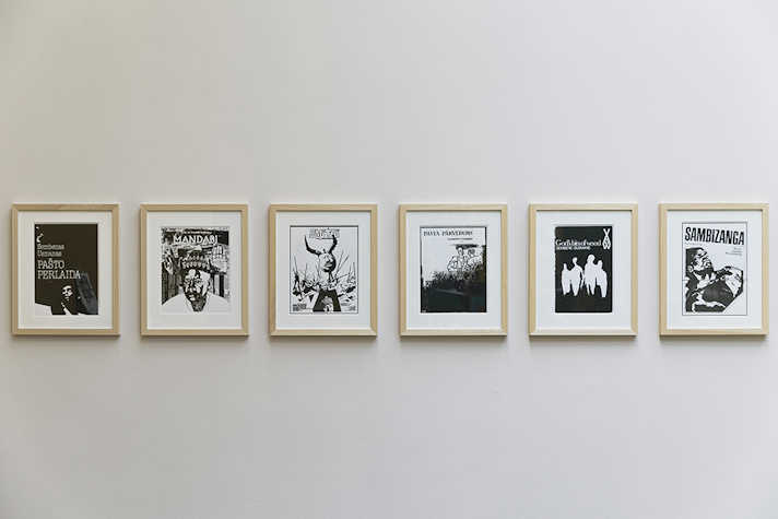 A white wall with six small wooden photo frames in a horizontal line. The frames each contain artwork in black and white.