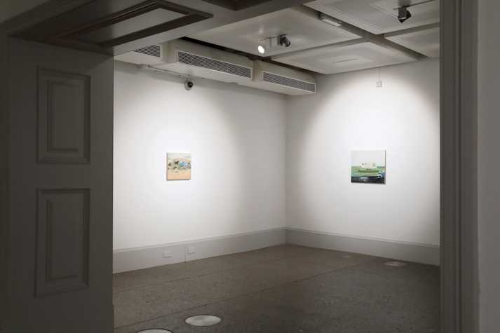 Two small oil paintings hang at a distance on white gallery walls