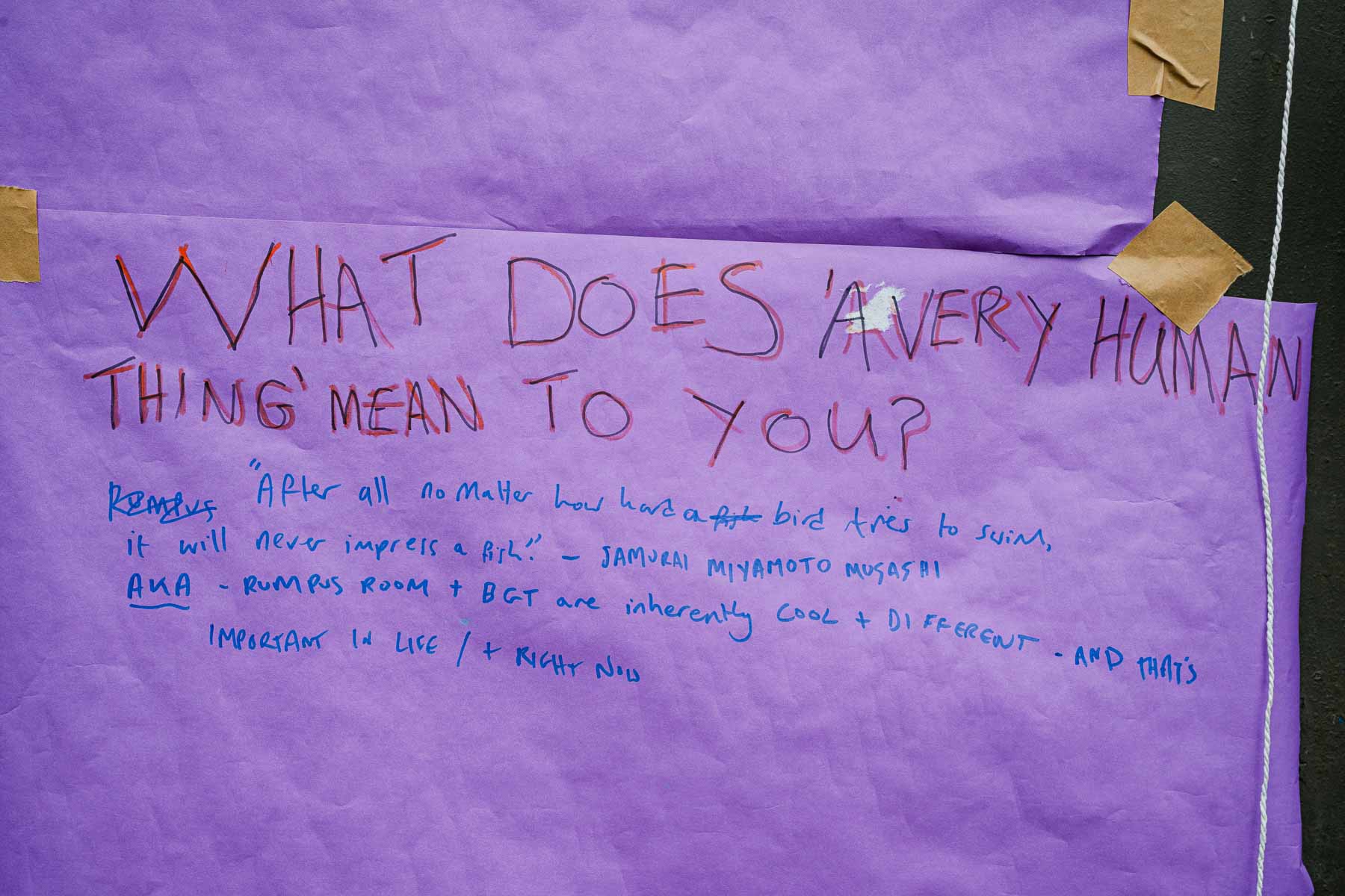 A hand-written sign on purple paper reads "What does 'a very human thing' mean to you?" with a handwritten quote and responses added below in marker pen.