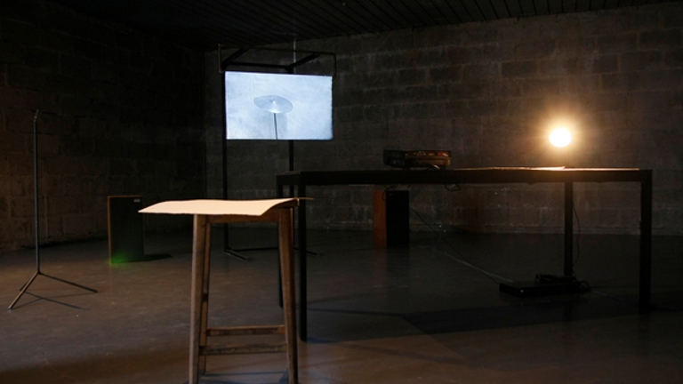 dark room with a wooden table and stool. in the background there is a small tv monitor 