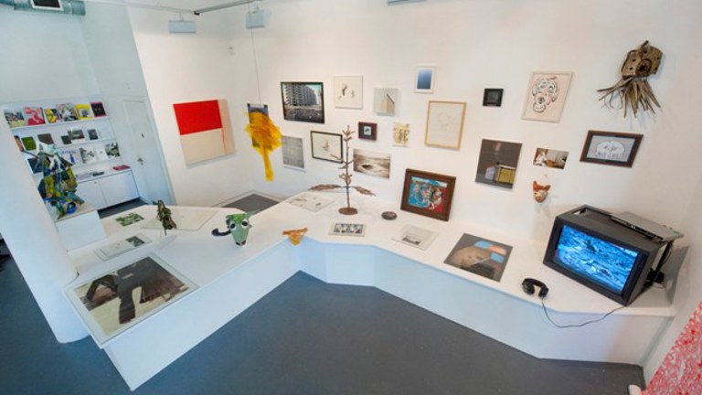 plethora of artworks and objects spread across a wall and a large bench/shelf that extends from the wall