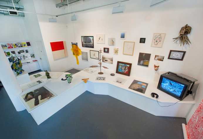 plethora of artworks and objects spread across a wall and a large bench/shelf that extends from the wall