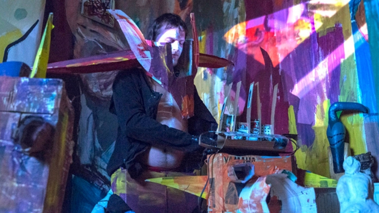 Photograph of a performance with figure in a cardboard and coloured paper installation 