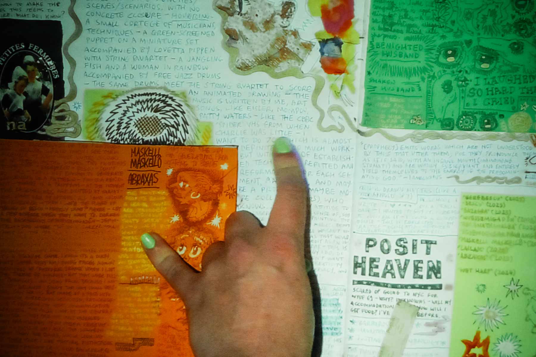 A performer speaks into a microphone beside a table with an open illustrated book, while a large colorful artwork is projected behind them.