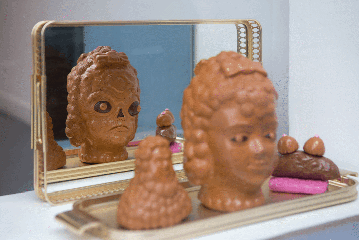 Clay sculptural head shapes on a gold coloured tray reflected in mirror
