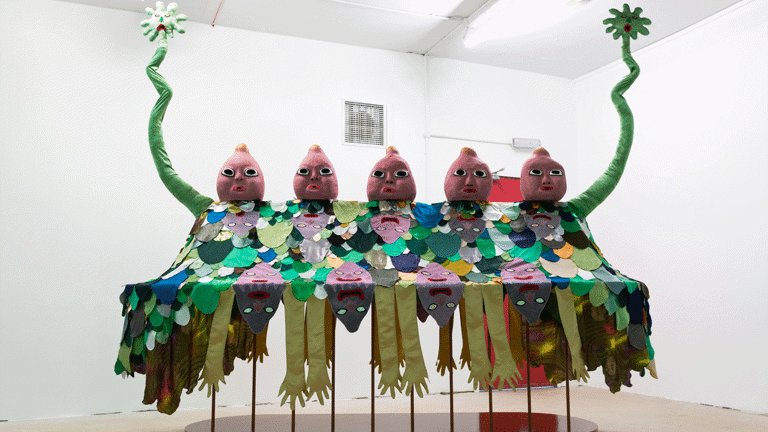 image of a large scale surreal sculpture with 5 baby-like heads, wiggling arms and a patchwork of fabric cut outs laid over it in the shape of cartoon-like arms and faces