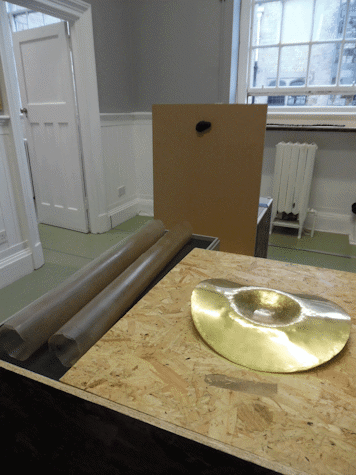 Two brown tubes next to cork and a golden metal object on top of it. In a white room with a window in the back wall.