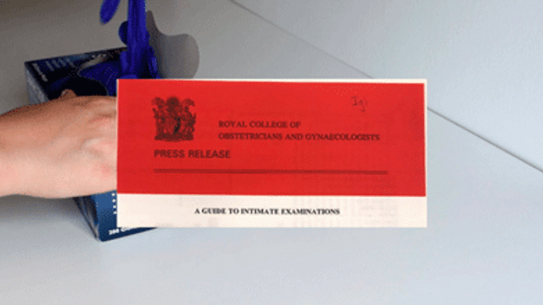 working still; red card reading 'press release, royal college of obstetricians and gynaecologists, a guide to intimate examinations' over a hand removing latex glove from box