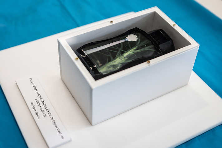A white box containing a painted coffee jar sits on top of a blue table covered with a blue tablecloth.