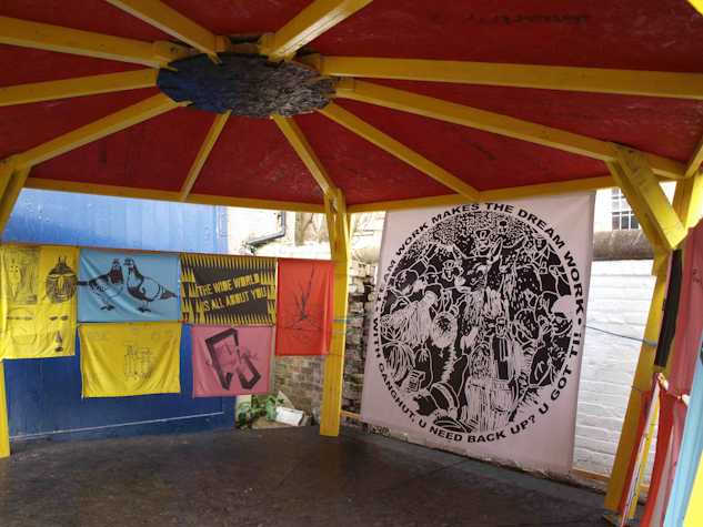 inside of a yellow and red gazebo. there are screen printed tapestries and flags hung in its perimeters.