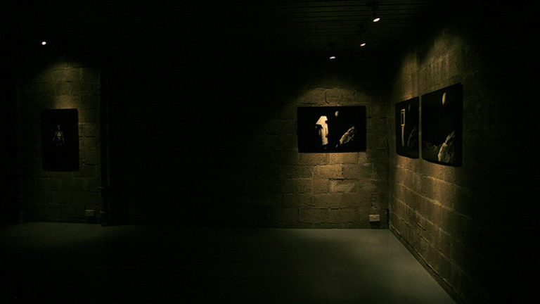 dimly lit room with brick walls. there are four works on the walls lit from above. 