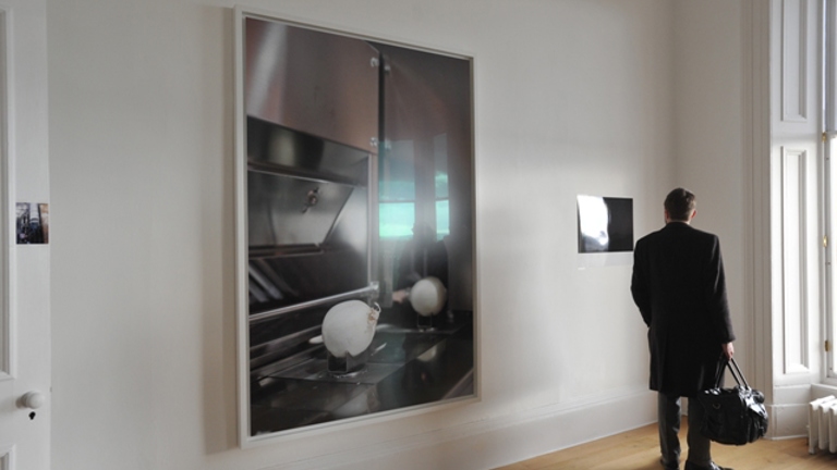 large framed image of an onion on a cooker. a man dressed in all black looks at a smaller photograph next to it.