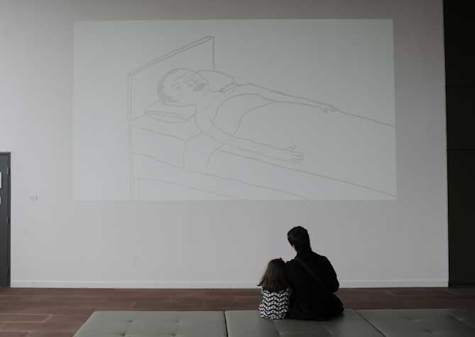 person and a child watching a projection on a wall. the projection shows an illustrated person lying in bed.
