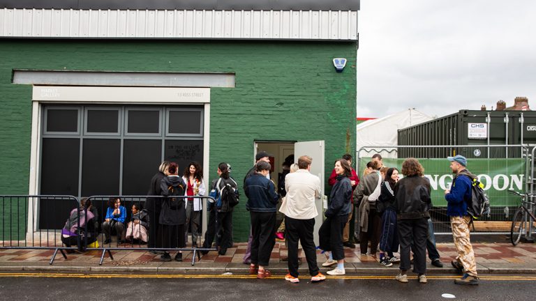A queue of visitors gathers outside Market Gallery's green-painted exterior on Ross Street, waiting to enter through the open door for the opening event.