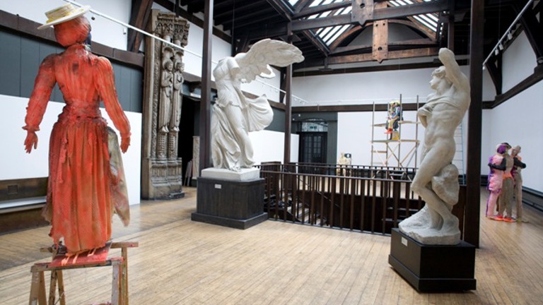 room with painted orange statue in foreground and two white marble statues in background