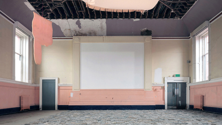 Installation view of the interior of a large room with a cobbled floor and a projection screen on the back wall