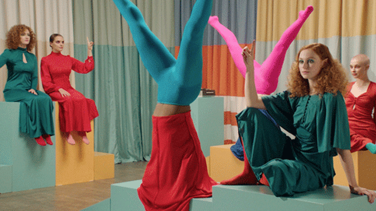  There are 4 actors in seated positions and two doing handstands. They are wearing very brightly coloured clothing. 