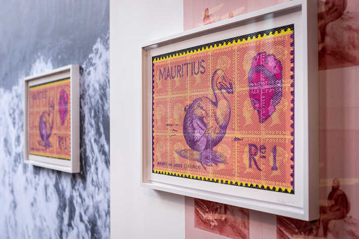 A photo of a wall with two white photo frames hanging from it. In each photo frame is a very large postage stamp with an image of a purple Dodo bird and the text 'R1' and 'Mauritius'.
