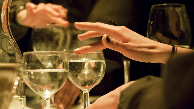 close up shot of wine glasses filled with water. above are two hands with their fingers on the rim of the glasses.