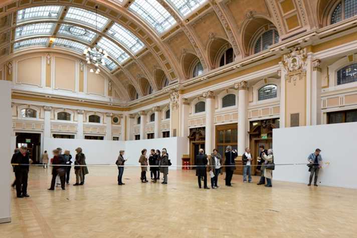 sculptural installation stretching horizontally across a large, ornate, victorian hall