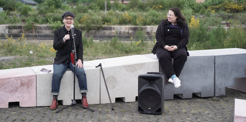 two people sitting on a wall, microphones in hand