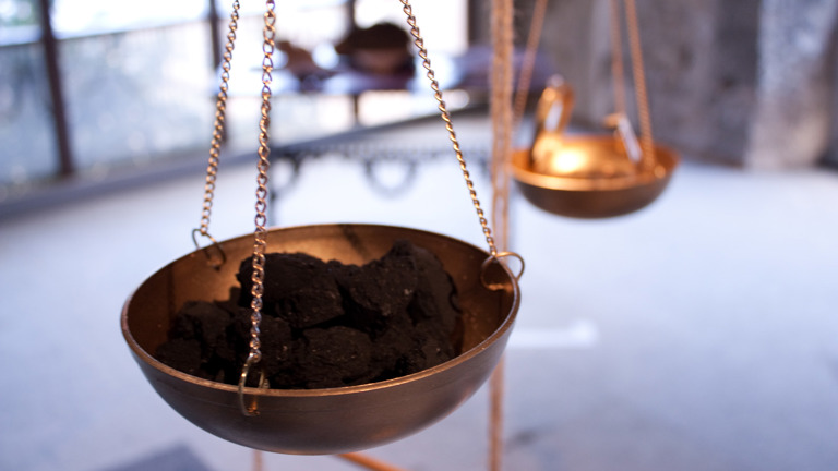 metal bowl hanging from three chains containing a dark coal-like material 