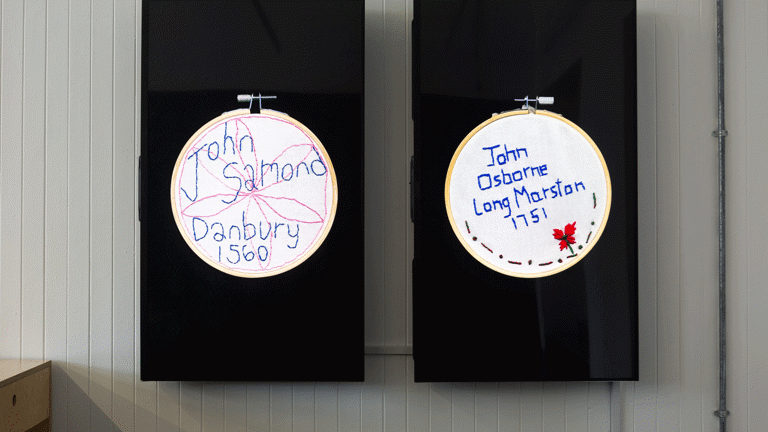 two TV screens mounted in portrait orientation show embroidery circles with the text 'John Samond Danbury 1560'