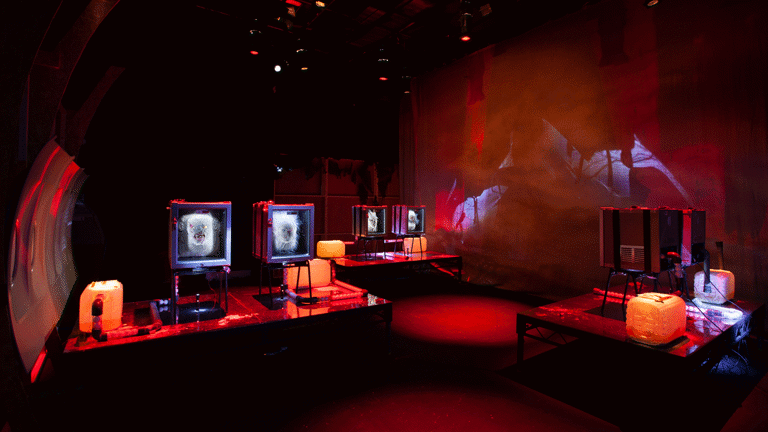 An image of jenkin van zyl's installation. There are 3 fridges holding mangled heads, panels from an aeroplane and eerie red lighting.