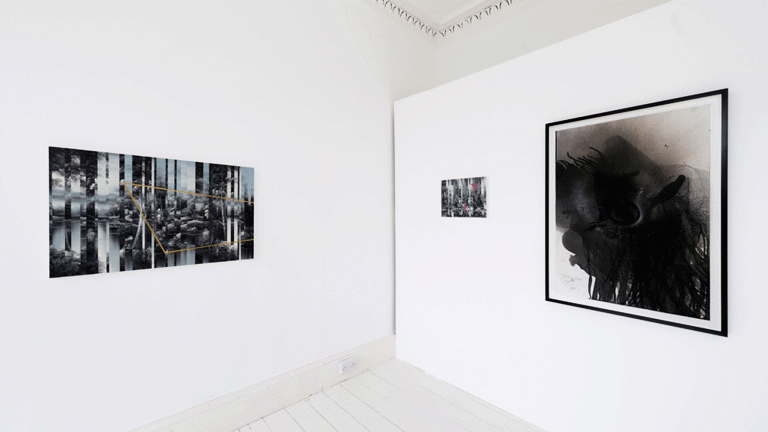 The corner of a white walled gallery with some photographic works visible on the walls 