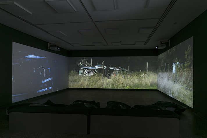 A dark room with three large connected screens. The screens on the centre and right display an image of an outdoor grassfilled area.