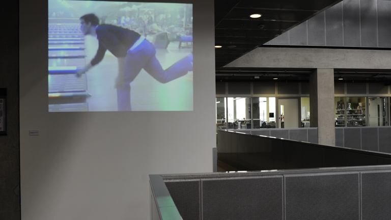 film projected in an office atrium space. the projection shows someone mid bowling