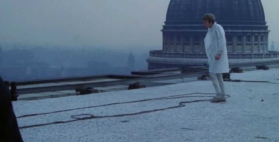 A film still showing a figure on a roof top with a large dome behind