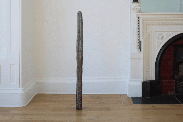 Next to the white fireplace there is a bronze figure of cactus. There is a white wall and wooden floors.