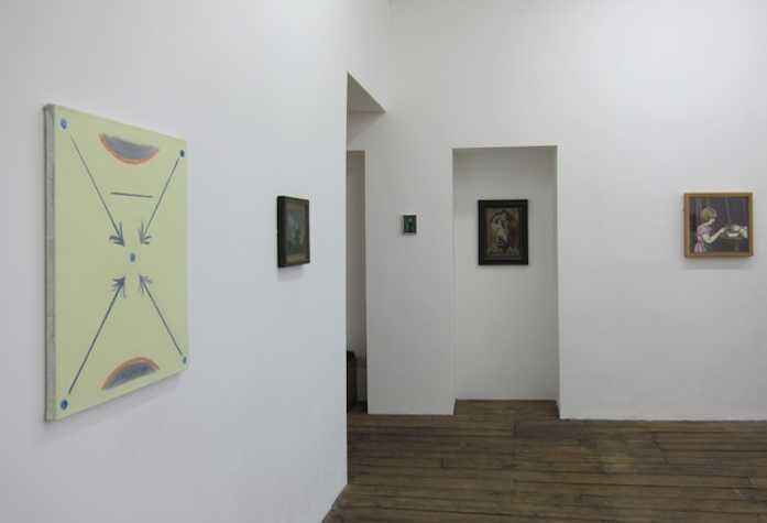 gallery install of works hung on white walls. closest to us is a canvas with  lines forming an 'X' framed at the top and bottom by lines and a semi circle.