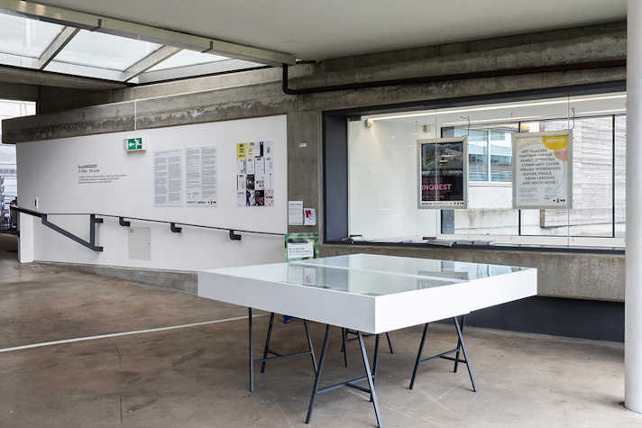 In a light and airy industrial space, artwork is displayed on white walls and there is a white display table.