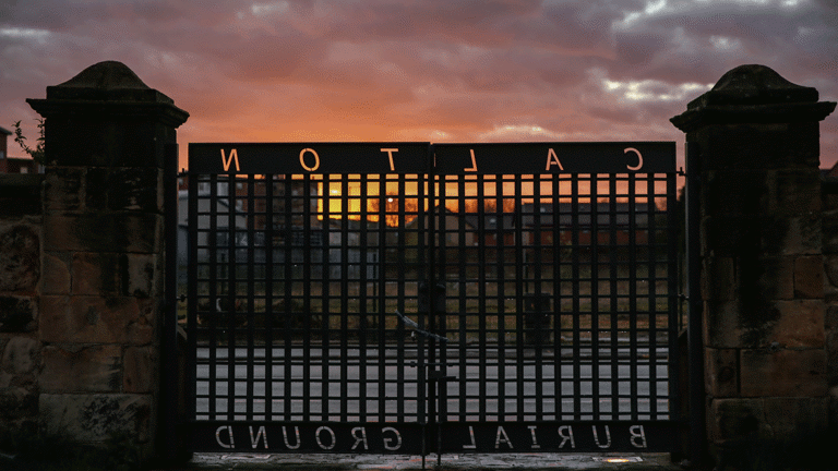 A picture of Calton Burial ground gates, in contrast with a orange and red sunset.