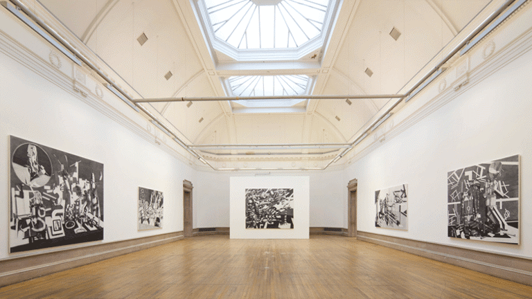 In a long long hallway, with wooden flooring and high ceiling, there are five large monochromatic artworks. Four of them are hung on the wall and one is placed at the end of the hall, put up on a temporary wall, placed ahead of the two doors at the end of the hall.