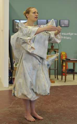 woman wearing a grey structural dress with her hands outstretched and curved to touch each other.