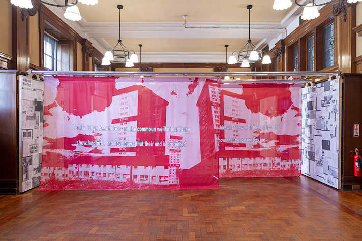 Printed pink and white fabric featuring text hangs across a wooden panelled room.