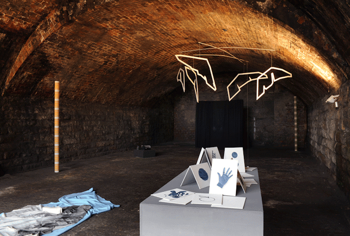 Vaulted basement with suspended neon sculpture in background, as well as other sculptural works