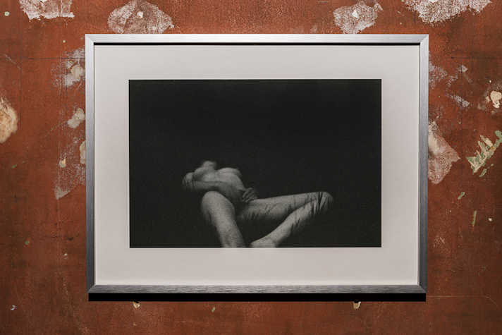 A framed artwork of a black and white nude figure. It is displayed on a red wall.