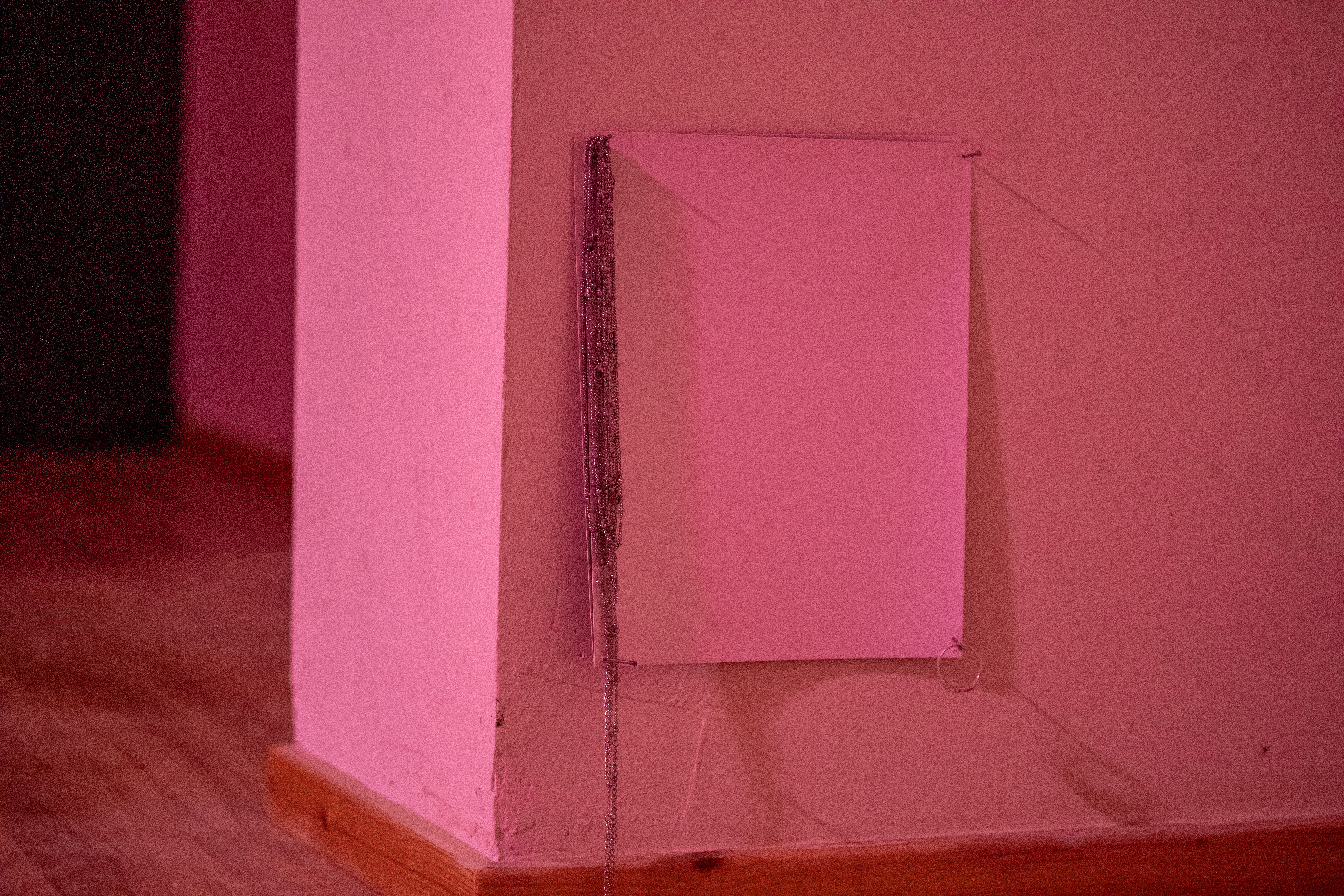 A small pink print or mirror mounted in a corner of Gulabi Gallery, with delicate silver chains and a ring draped down its edge.